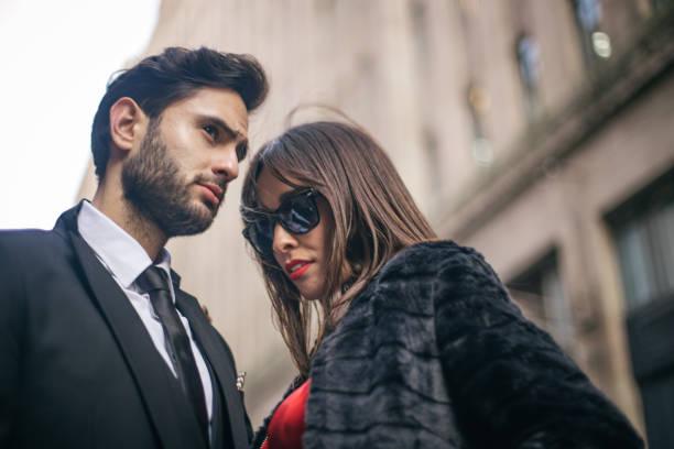 Couple élégant en vêtements tendance, homme en costume et femme en manteau et lunettes de soleil en ville