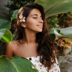 Femme avec accessoire cheveux fleur tropicale au milieu de grandes feuilles vertes