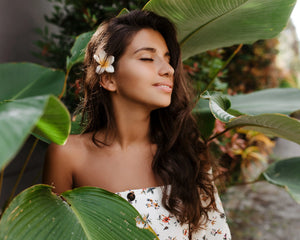 Femme avec accessoire cheveux fleur tropicale au milieu de grandes feuilles vertes