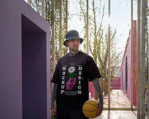 Homme portant un t-shirt imprimé et bob noir, tenant un ballon de basket, dans un décor violet moderne.