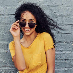 Femme souriante en t-shirt jaune et lunettes de soleil devant un mur gris, mode été Réunion
