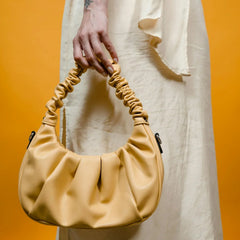 Sac à main jaune plissé porté à la main, fond orange, mode femme tendance