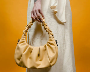 Sac à main jaune plissé porté à la main, fond orange, mode femme tendance