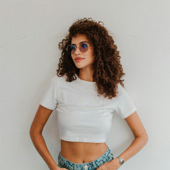 Femme avec cheveux bouclés portant un crop top blanc et lunettes de soleil, style décontracté