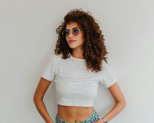 Femme avec cheveux bouclés portant un crop top blanc et lunettes de soleil, style décontracté