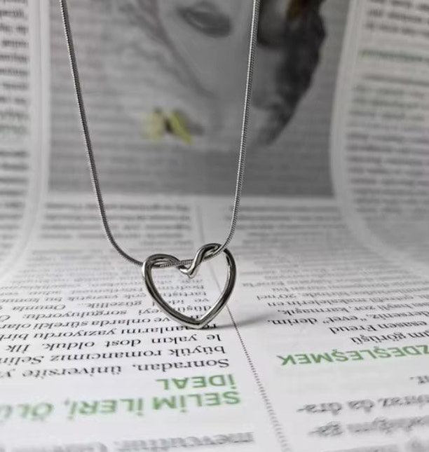 Collier pendentif cœur argenté minimaliste sur fond de journal, bijou femme élégant