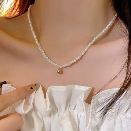 Collier femme perles fines avec pendentif doré, porté sur haut blanc élégant