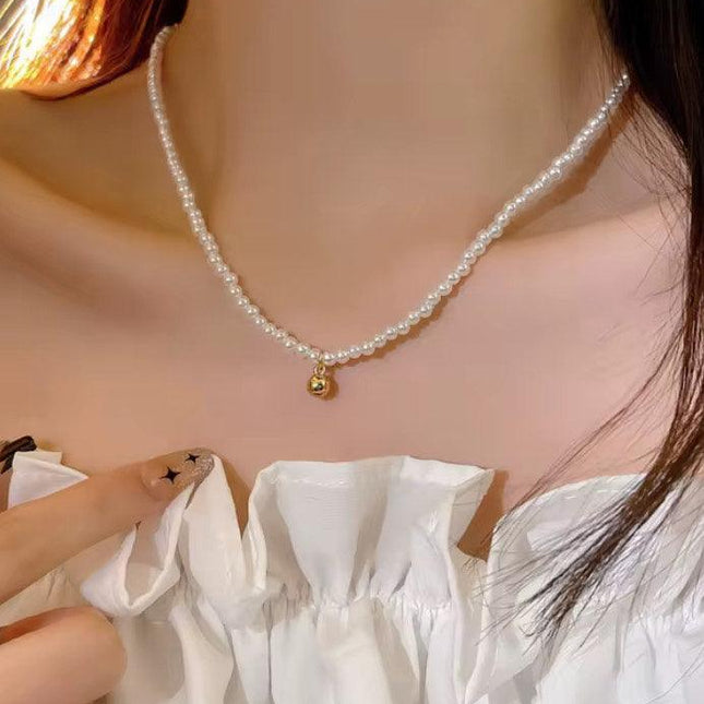 Collier femme perles fines avec pendentif doré, porté sur haut blanc élégant