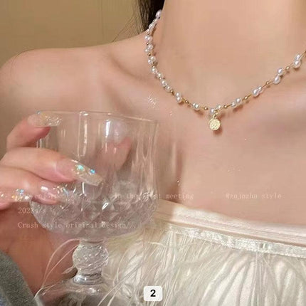 Femme portant un collier ras du cou perles blanches dorées, robe bustier, main tenant un verre élégant