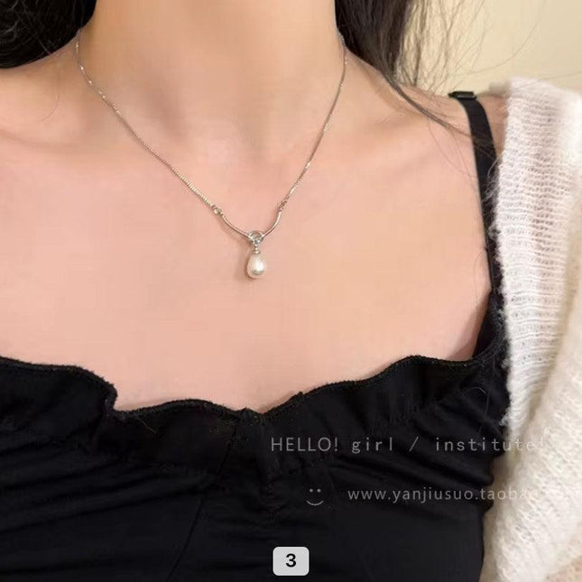 Collier argenté avec pendentif perle blanche porté sur un haut noir féminin