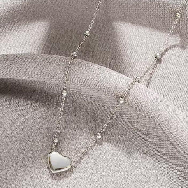 Collier en argent avec pendentif cœur nacré et perles rondes, sur fond tissu gris.