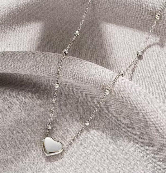 Collier en argent avec pendentif cœur nacré et perles rondes, sur fond tissu gris.