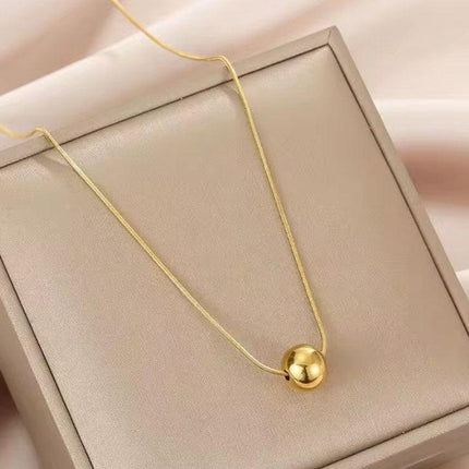 Collier femme doré avec pendentif boule, exposé sur un coffret beige élégant