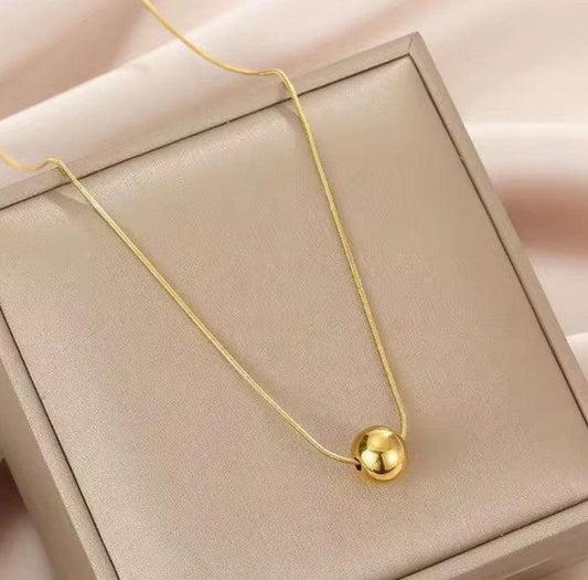 Collier femme doré avec pendentif boule, exposé sur un coffret beige élégant