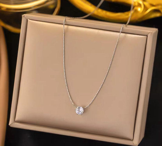 Collier fin argenté avec pendentif solitaire rond brillant, présenté sur écrin beige.