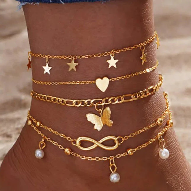 Lot de bracelets chevilles dorés avec motifs étoile, cœur, papillon et perles, sur pied féminin