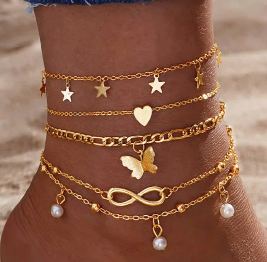 Lot de bracelets chevilles dorés avec motifs étoile, cœur, papillon et perles, sur pied féminin