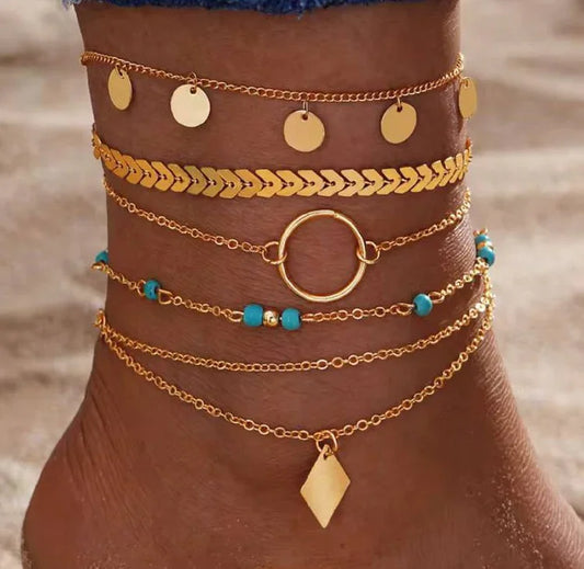 Cheville ornée de bracelets dorés fantaisie et perles turquoise, style plage tendance.