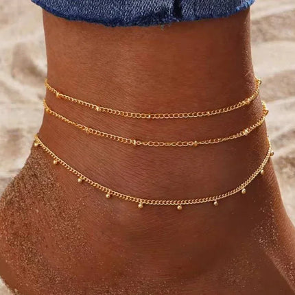Cheville ornée de bracelets dorés fins sur sable, bijou d'été femme tendance