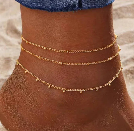 Cheville ornée de bracelets dorés fins sur sable, bijou d'été femme tendance