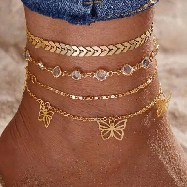 Cheville ornée de bracelets chaîne dorés avec pendentifs papillon, sur la plage.