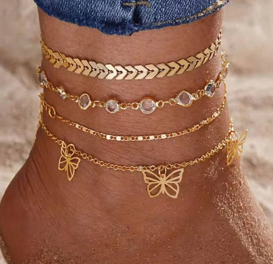 Cheville ornée de bracelets chaîne dorés avec pendentifs papillon, sur la plage.