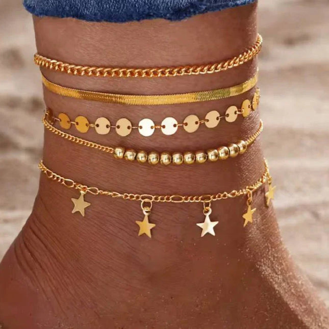 Cheville ornée de bracelets de cheville dorés avec pampilles étoiles sur fond de sable
