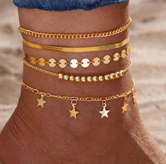 Cheville ornée de bracelets de cheville dorés avec pampilles étoiles sur fond de sable