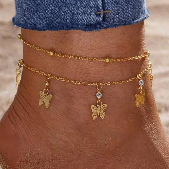 Cheville ornée de deux bracelets dorés avec pendentifs papillon et strass, plage, mode femme.