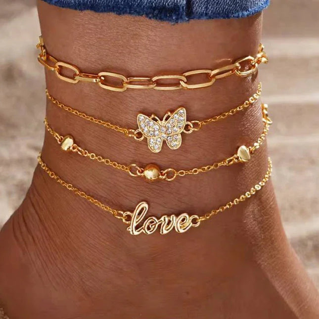 Cheville ornée de bracelets chaîne dorés, pendentif papillon et inscription love, plage.