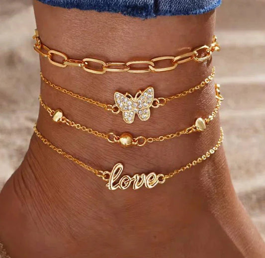 Cheville ornée de bracelets chaîne dorés, pendentif papillon et inscription love, plage.